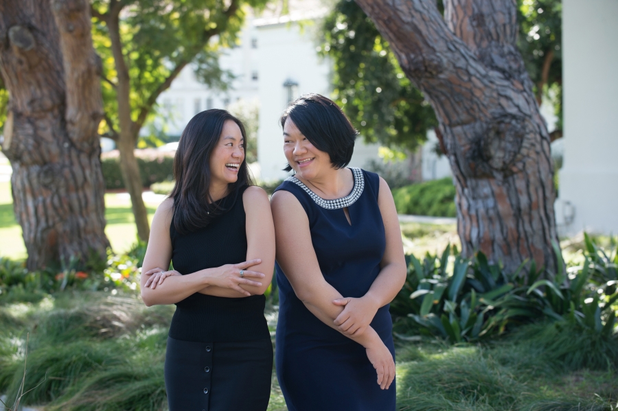 Jennifer Li Shen and Way-Ting Chen, Co-Founders of Blue Garnet, in elegant black sleeveless dresses. They are looking at each other and smiling, surrounded by trees and greenery