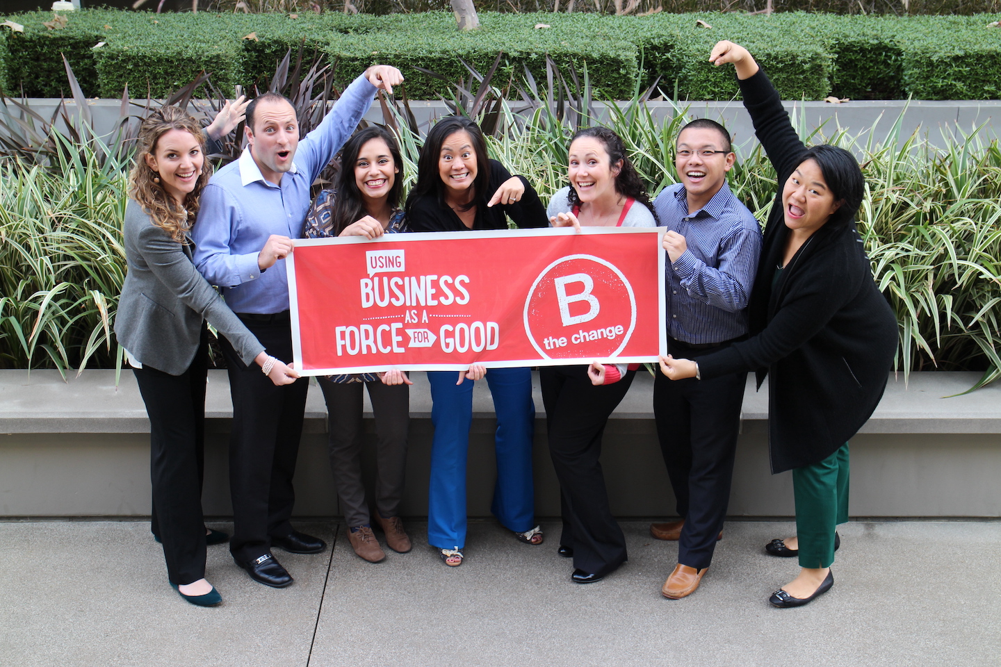 Blue Garnet team members celebrate becomine a B Corp as they point to a red and red banner