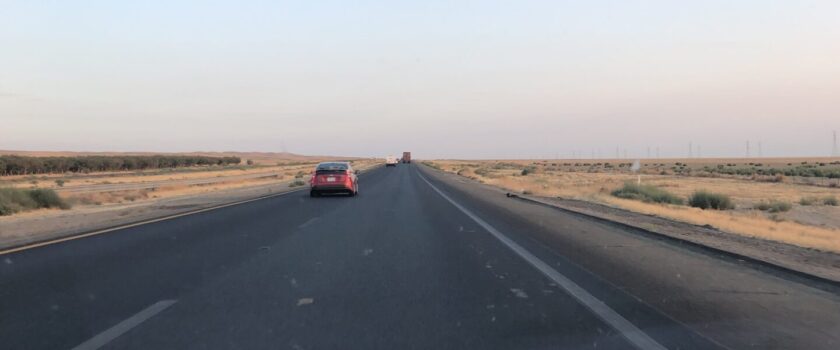 California highway at dawn, with one red car up ahead