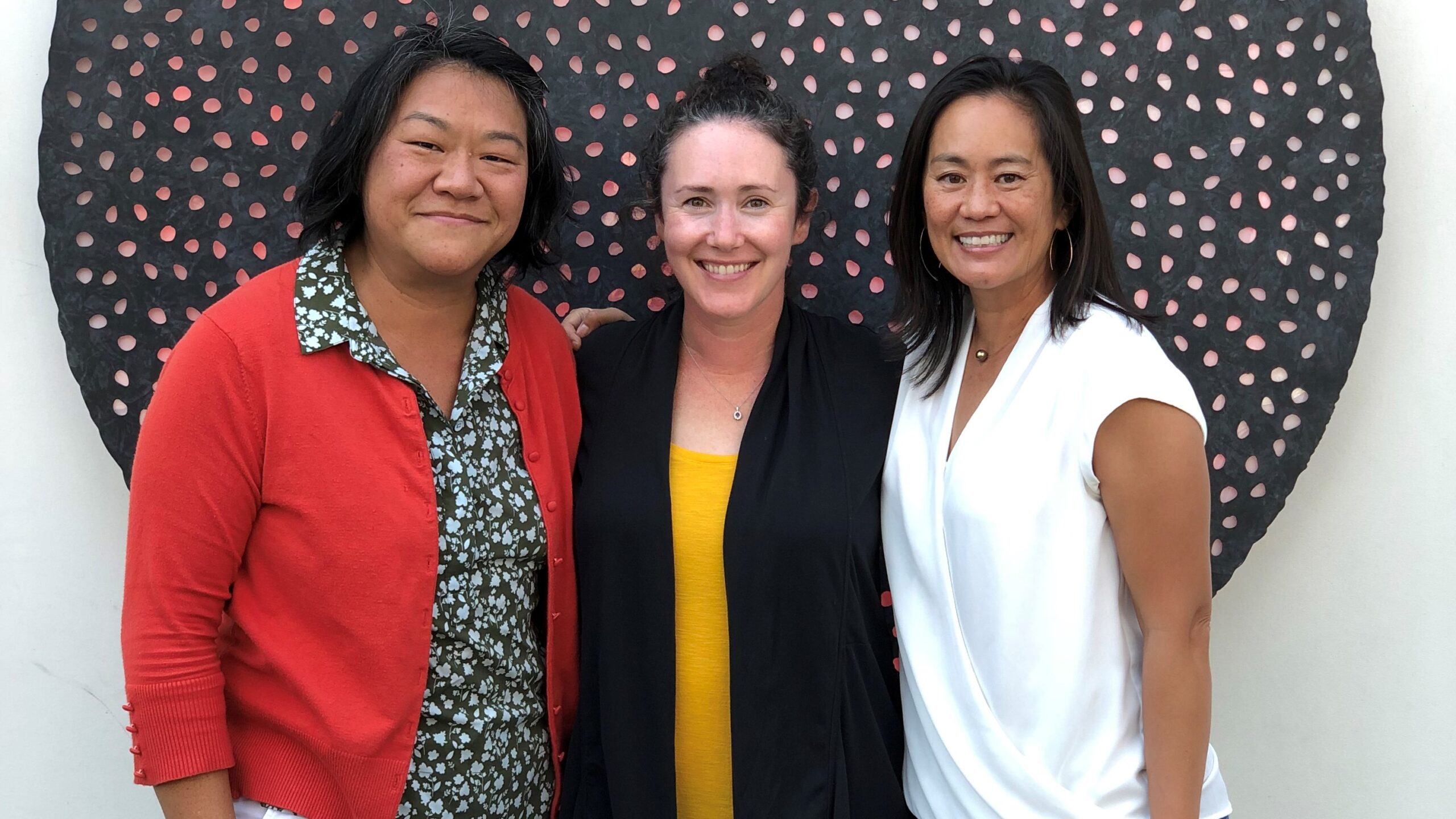 Three women smiling in front of a polka-dot wall