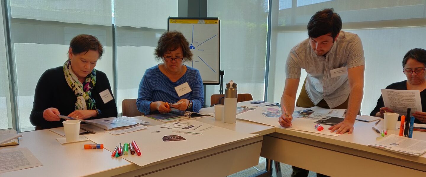 Four people are gathered around an L-shaped table doing a craft activity