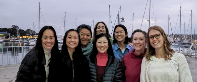 Group photo of smiling women with marina and boats in background