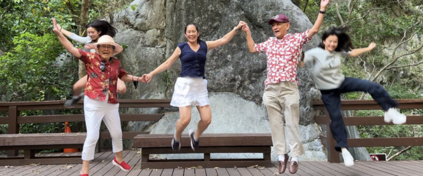 Five people holding hands and jumping in front of a waterfall