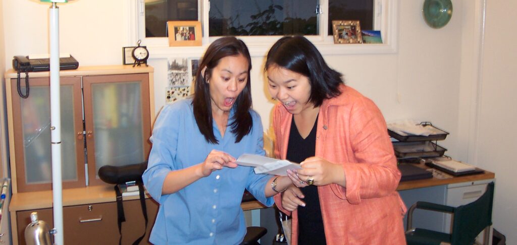 Two women look at a piece of paper in joyful shock.