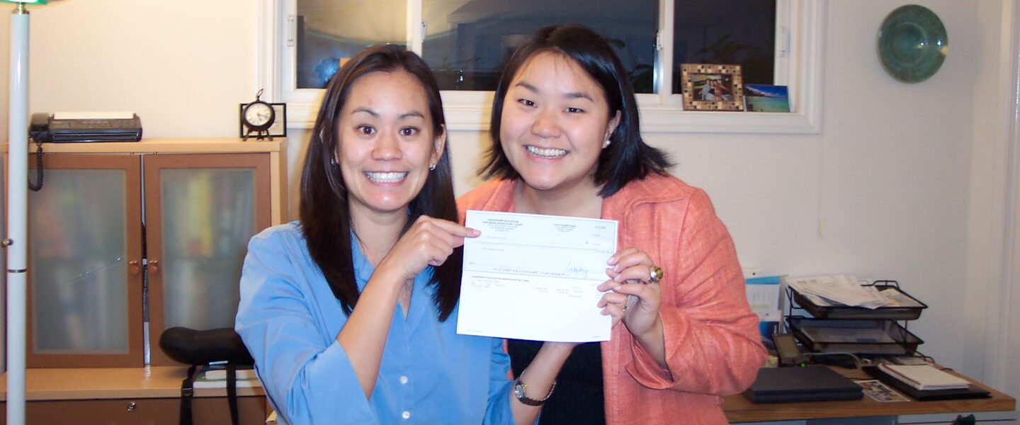 Two women hold up a paycheck and smile.