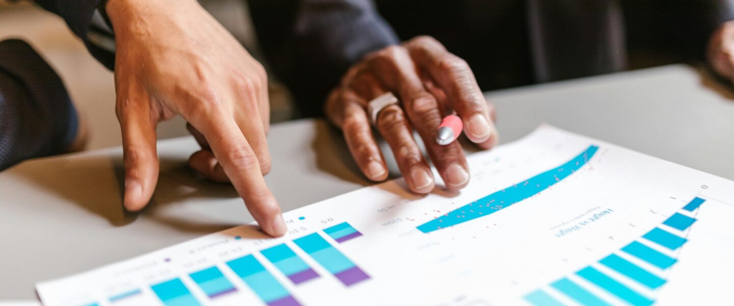 Hands pointing to sheet of paper with charts on table